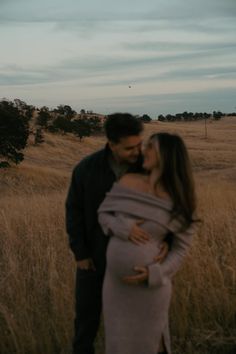 a pregnant couple cuddle in a field at sunset