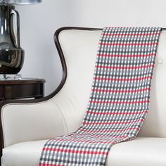 a white chair with a red and black plaid blanket on it's back next to a lamp