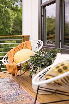 two white chairs sitting on top of a wooden floor next to a rug and potted plants