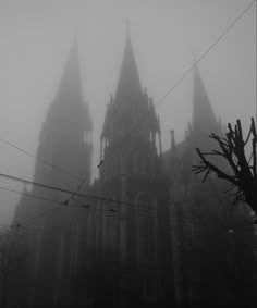 an old gothic church in the fog with power lines running through it's foreground