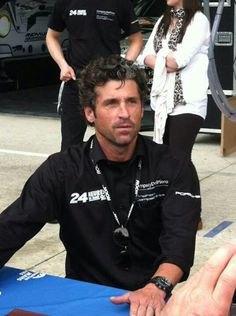 a man sitting at a table with his hand on the ground and two people standing behind him