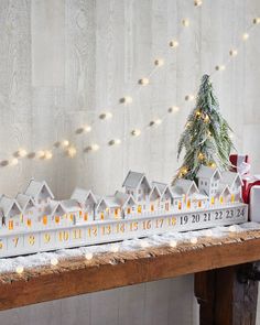 a wooden table topped with a christmas tree and small white houses next to a lit up fir tree