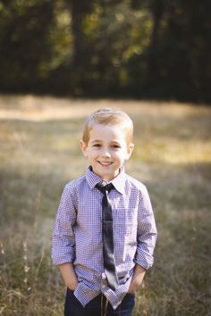 a young boy wearing a tie and standing in the middle of a field with tall grass