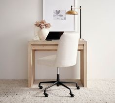 a desk with a laptop on it in front of a white wall and flower vase