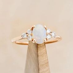 a white opal and diamond ring sitting on top of a wooden stand