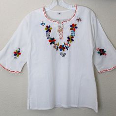 a white shirt with colorful flowers on it hanging from a hook in a room next to a wall