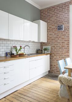 a kitchen with white cabinets and wooden floors next to a brick wall in the background