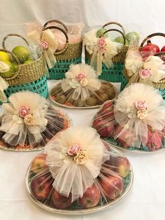 four baskets filled with fruit on top of a white table cloth covered plated in tulle