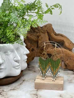 a pair of green earrings sitting on top of a wooden stand next to a potted plant