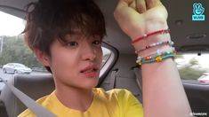 a young man in a car with bracelets on his wrist and wearing a yellow shirt