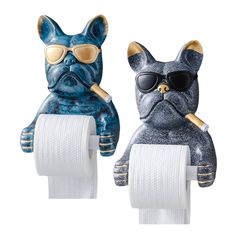 two ceramic dogs with sunglasses on top of toilet paper holders, one holding a roll of toilet paper and the other wearing shades