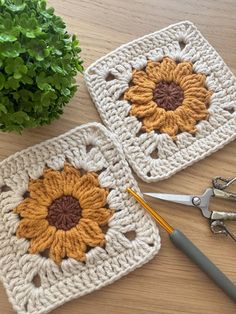 two crocheted coasters with flowers on them next to scissors and a plant