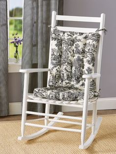 a white rocking chair with black and white pillows on it in front of a window