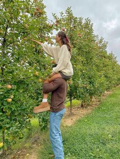 a man carrying a woman on his back picking apples from an apple tree in the orchard