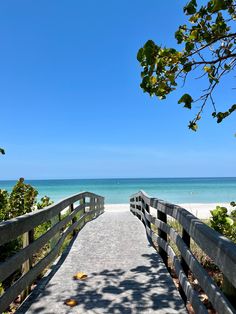 a wooden walkway leading to the beach and ocean with trees on either side that lead into the water