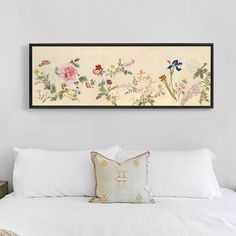 a white bed topped with pillows next to a framed painting