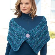 a woman wearing a blue sweater with a knitted shawl around her shoulders and buttons on the front