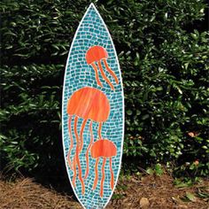 a blue and orange surfboard with two jellyfish on it's side in front of some bushes