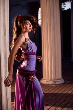 a woman in a purple dress standing next to columns