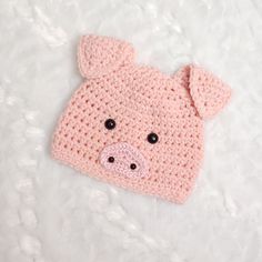 a pink knitted pig hat laying on top of a white blanket with black eyes