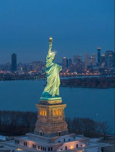 the statue of liberty is lit up at night in front of the cityscape