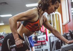 a woman working out in the gym with dumbbells on her chest and looking down