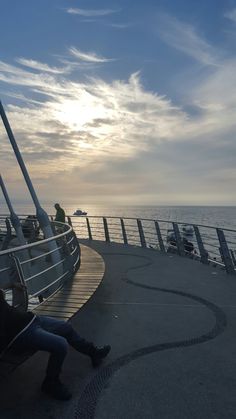 two people sitting on the edge of a boat looking out over the water at sunset