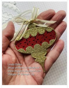 a hand holding an ornament in the shape of a red and gold heart