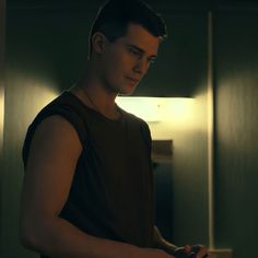 a man standing in front of a mirror looking at his cell phone while wearing a sleeveless shirt