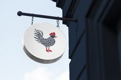 a sign hanging from the side of a building with a rooster on it's back