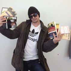 a man holding up two books in one hand and wearing a beanie on the other