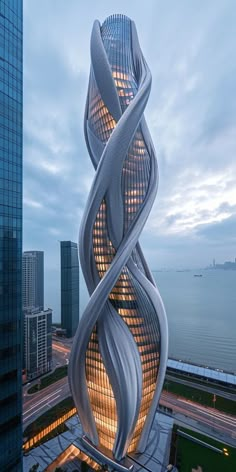 a tall building with a spiral design on the front and side, next to a large body of water