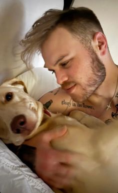 a man laying in bed next to a dog with tattoos on his arm and chest