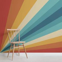 a wooden chair sitting in front of a wall with a rainbow pattern on the wall