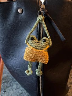 a crocheted frog key chain hanging from a black leather handbag on a table