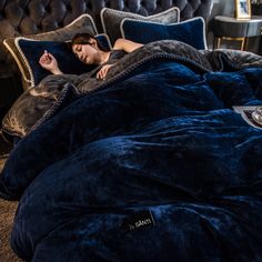 a woman laying on top of a blue comforter in a bed covered with pillows