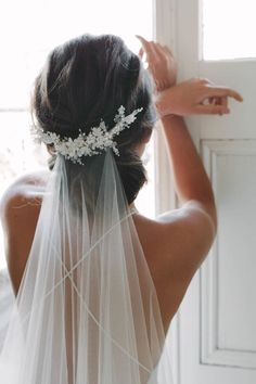 the back of a bride's head wearing a veil with flowers and pearls on it