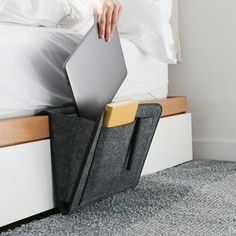 a bed with an open laptop on it and a person reaching for the pillow in the background