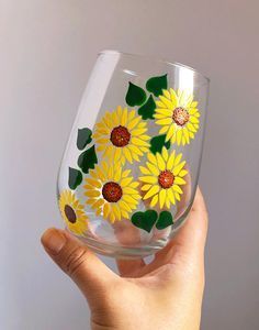 a hand holding up a wine glass with yellow flowers painted on the side and green leaves