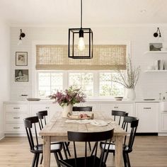 a dining room table with black chairs in front of a window and white cupboards