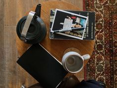 a wooden table topped with a cup of coffee next to a magazine and a camera