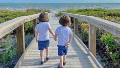 two young boys walking down a wooden walkway towards the ocean