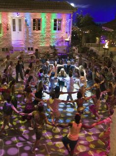 a large group of people doing various activities in front of a building with colored lights