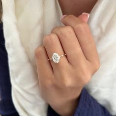 a woman's hand with a diamond ring on her left hand, wearing a white shirt