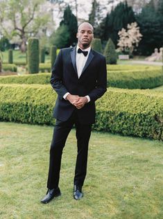 a man in a tuxedo poses for a photo on the lawn at his wedding