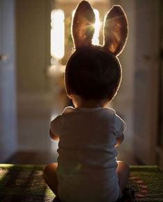 a little boy sitting on the floor with his back turned to the camera, wearing a bunny ears headband