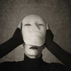 a person with a mask on their head and hands over their ears, covering the face