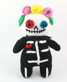 a crocheted skeleton doll with flowers on its head and eyes is posed in front of a white background