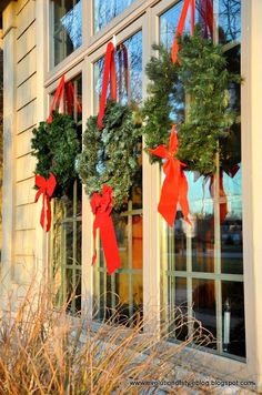 three wreaths are hanging on the windowsill in front of a house with red bows