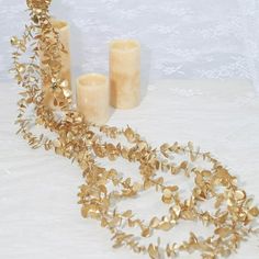 two candles and some gold leaves on a white table cloth next to it is a candle holder with three votives in the background